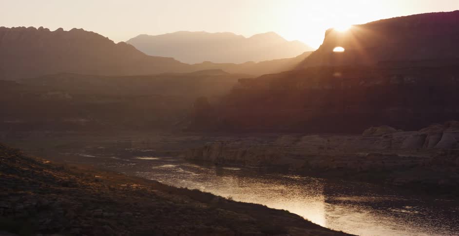 Golden sunset shines through a natural rock arch over a tranquil river in a vast desert canyon