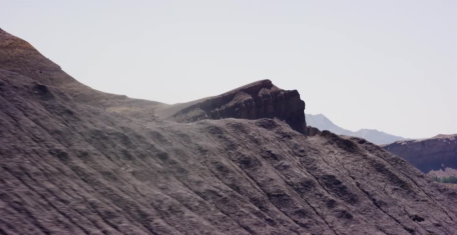 An aerial tracking shot moves across a vast, eroded grey rock formation in a barren desert landscape