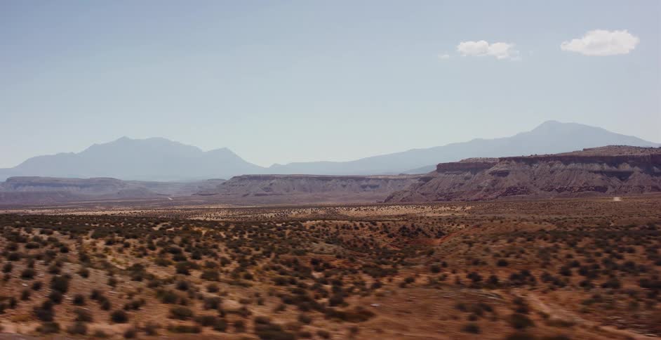 A beautiful moving shot travels across a vast desert landscape with mesas and mountains in the distance on a clear day