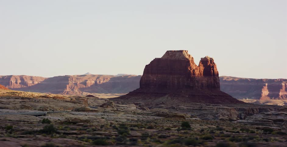 A majestic red rock butte is revealed in a slow pan across a vast desert canyon landscape at golden hour