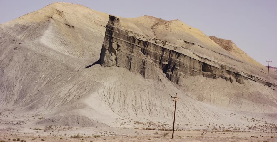 A slow zoom reveals a striking, angled rock formation standing tall in a barren desert landscape