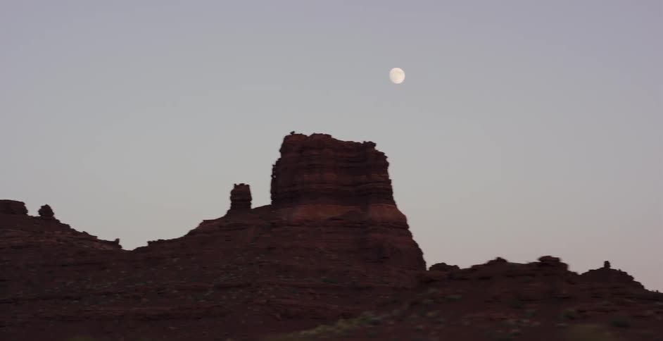 Driving shot past a silhouetted red rock mesa at twilight with a bright full moon overhead