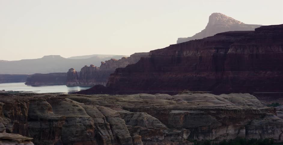 A majestic reveal shot from a moving vehicle captures the vast, layered rock formations and the serene river winding through a stunning canyon landscape