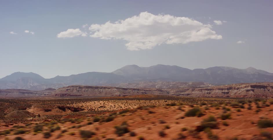 A tracking shot reveals the vast red desert landscape of the American Southwest, with distant mountains under a clear blue sky