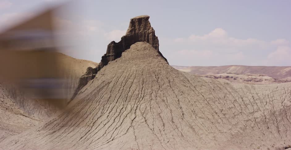 A cinematic pan reveals the stark and desolate beauty of a desert badlands landscape, focusing on a unique eroded rock formation