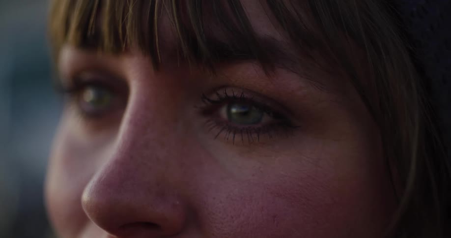 An intimate close-up of a woman's green eyes looking thoughtfully into the distance as she blinks slowly
