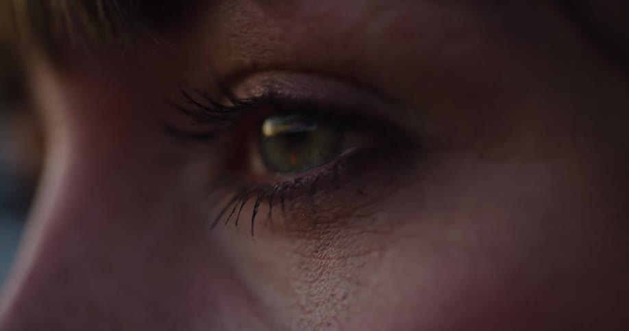 An intimate, moody extreme close-up of a woman's green eye looking intently and blinking