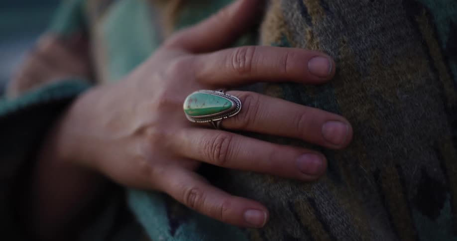 Close-up of a hand with a silver and turquoise ring resting on a patterned wool blanket