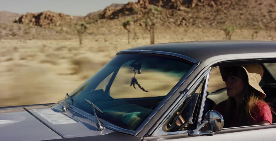 Close-up of a woman in a sun hat driving a classic car through a sunny desert landscape