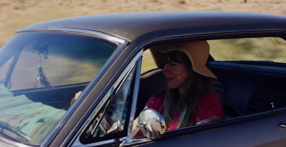Side view of a carefree woman in a straw hat driving her classic car on a sunny road trip through the desert