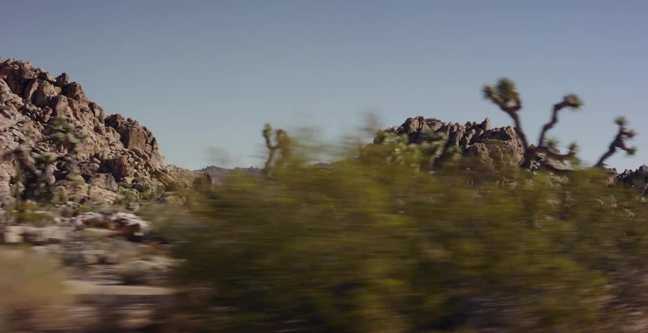 A fast-moving drive-by view of the rocky desert landscape and Joshua trees under a clear blue sky