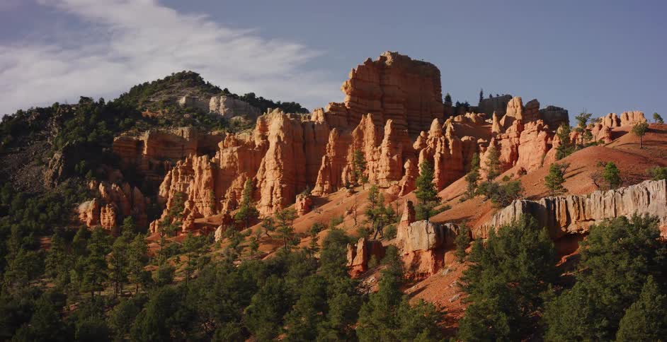 Sunlight gently illuminates the iconic red rock hoodoos and pine-covered hills of a western canyon