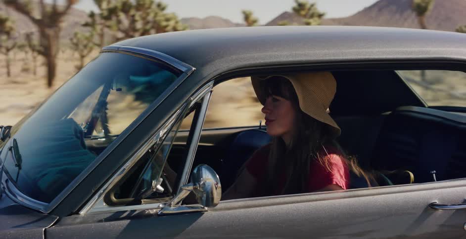 A stylish woman in a sun hat drives a classic car through the picturesque desert landscape on a sunny day
