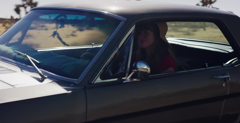 A young woman wearing a hat enjoys a scenic drive in a classic muscle car through the sunny desert