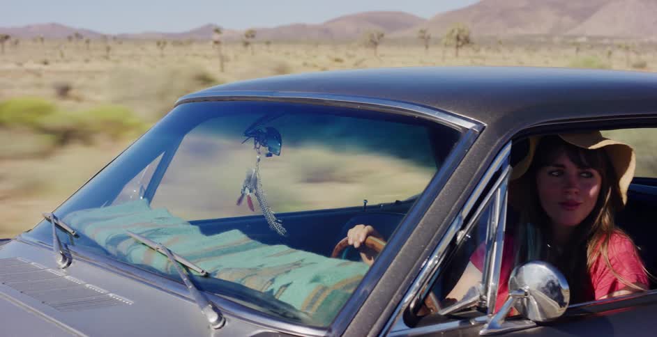 A stylish woman in a sun hat drives her classic muscle car on a scenic road trip through the sunny desert