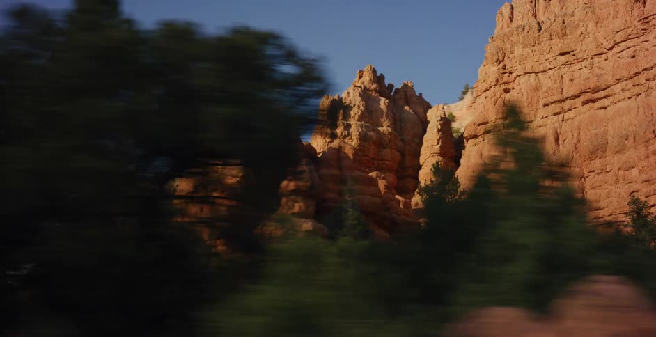 A scenic drive past majestic red rock formations and hoodoos in a canyon, illuminated by golden sunlight