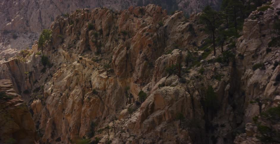 A slow, sweeping pan reveals the rugged, rocky cliffside of a vast mountain range