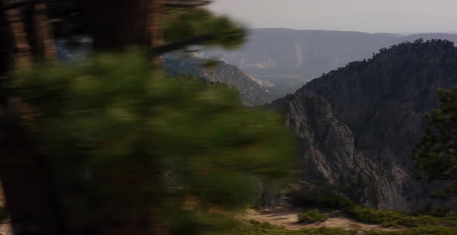A stunning tracking shot reveals a vast and rugged mountain landscape with deep canyons and rocky cliffs