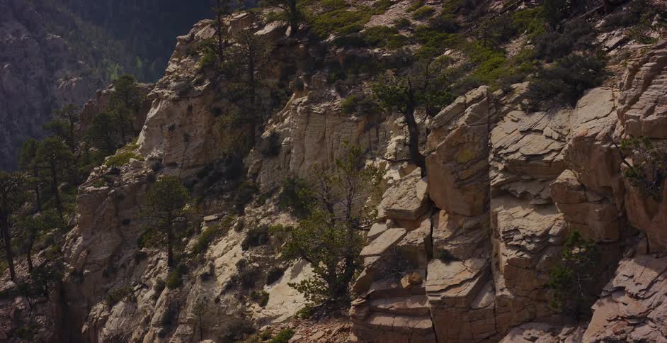 An aerial shot slowly pulls back from a rugged, sun-drenched cliffside revealing its rocky textures and sparse vegetation