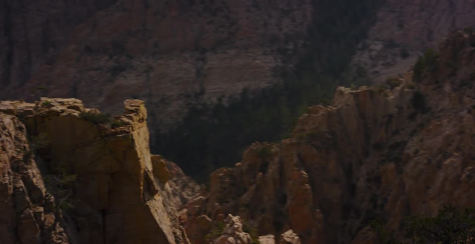 A slow pan across a rugged, sunlit cliff face reveals the vast, hazy expanse of a mountain canyon