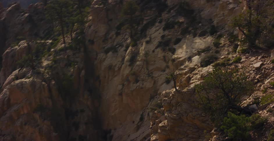An immersive aerial shot pans slowly across the sun-drenched, rugged cliffs of a vast mountain canyon