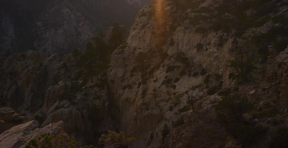 The golden hour sun glows over a rugged mountain landscape as the camera pans down the rocky canyon