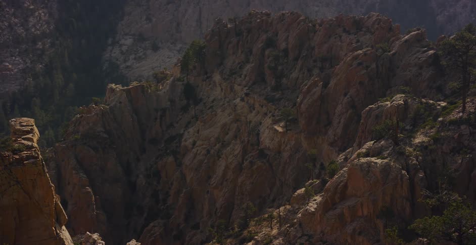 A slow pan reveals the vast and rugged beauty of a sunlit mountain canyon dotted with pine trees