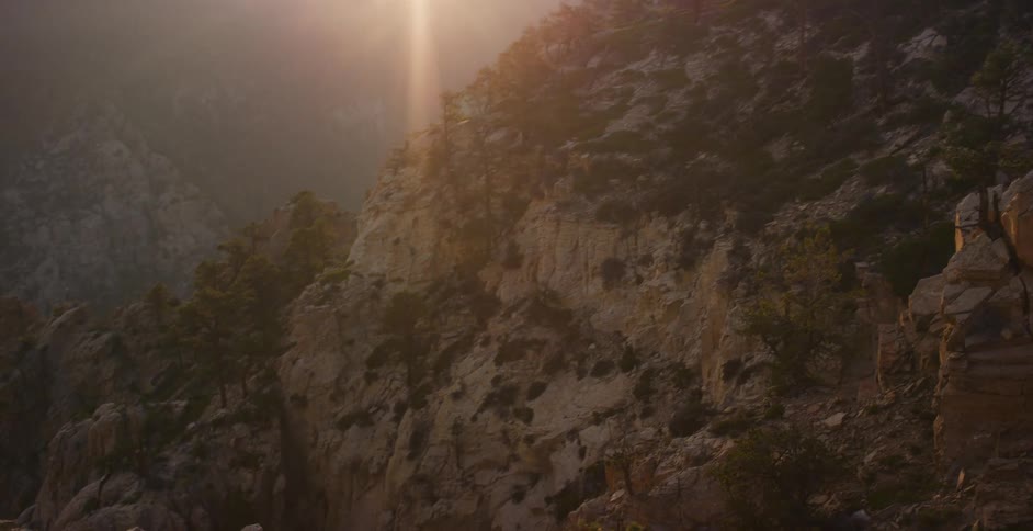 A slow pan reveals a majestic mountain range as the golden hour sun illuminates the rugged canyon below