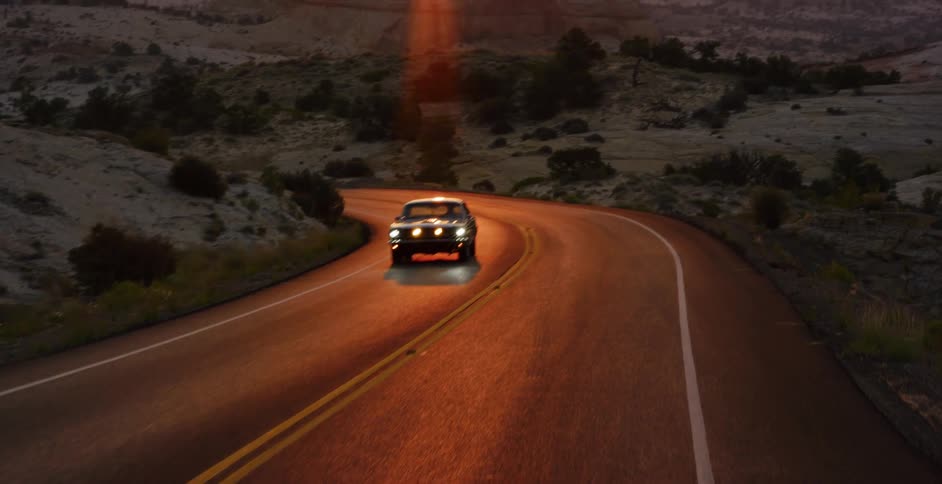 A classic car drives along a winding desert road at sunrise, revealing a beautiful, expansive landscape