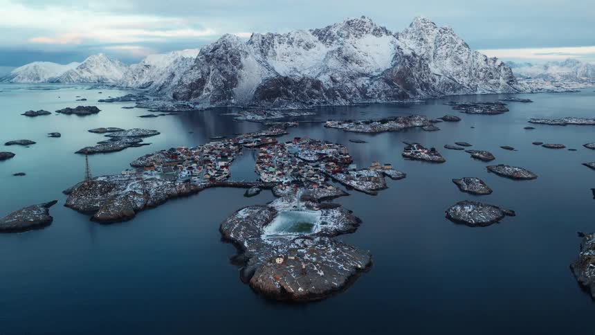 Stunning aerial view reveals the snowy fishing village of Henningsvaer and its football pitch nestled among islands and majestic mountains in Norway