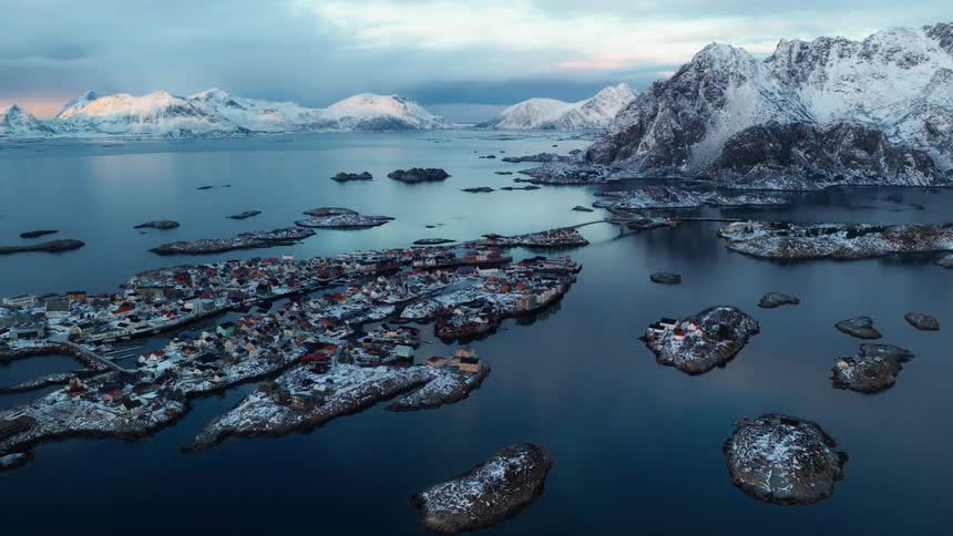 Stunning aerial panorama of a snowy coastal village on scattered islands surrounded by majestic mountains and calm waters at twilight