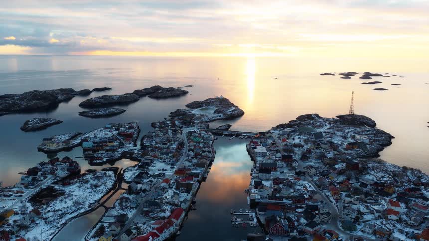 A majestic aerial view captures a snowy Nordic fishing village built on a cluster of islands during a beautiful golden sunset