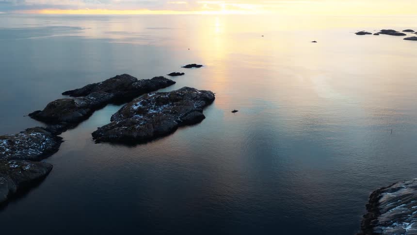 Stunning aerial view of a snowy, rocky archipelago in a calm sea during a magnificent golden sunrise