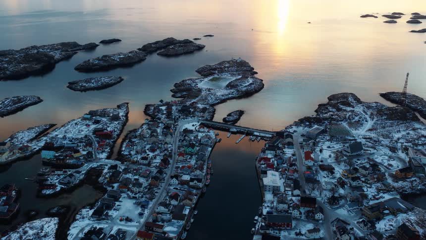 An aerial view reveals a picturesque snow-covered fishing village scattered across rocky islands as the golden sun sets over the calm ocean