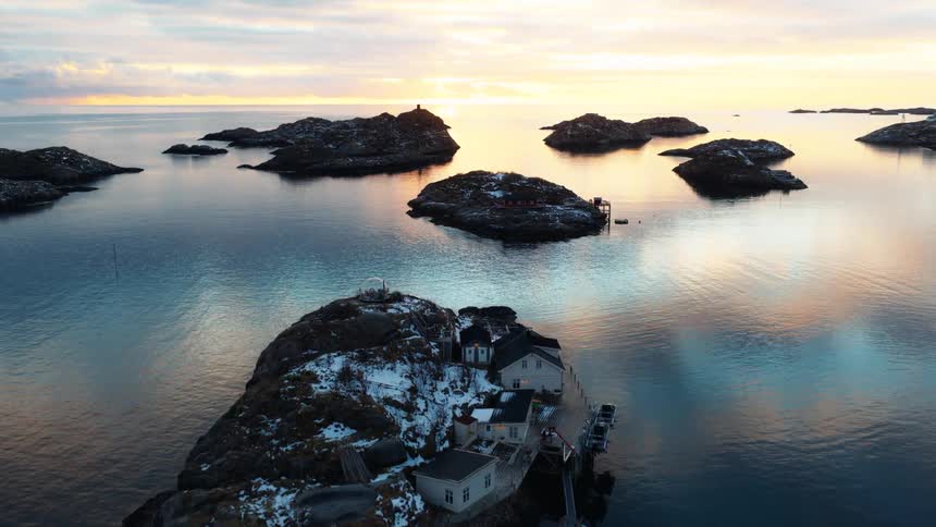 A serene aerial shot slowly reveals a remote Nordic archipelago with snow-covered islands and houses during a tranquil sunrise