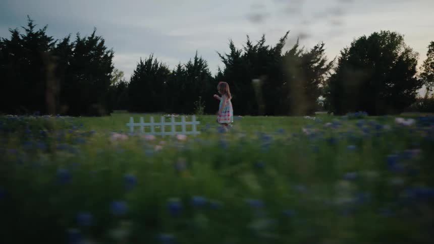 A little girl in a summer dress runs through a beautiful field of bluebonnets at twilight in slow motion