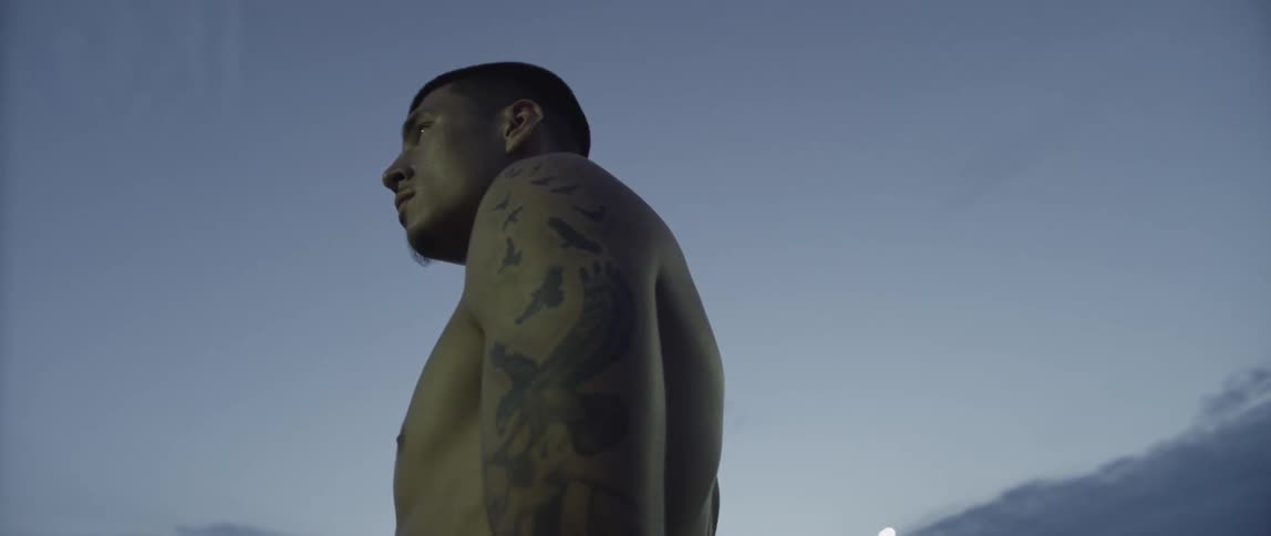 Tattooed young man stands shirtless on a sports field at night