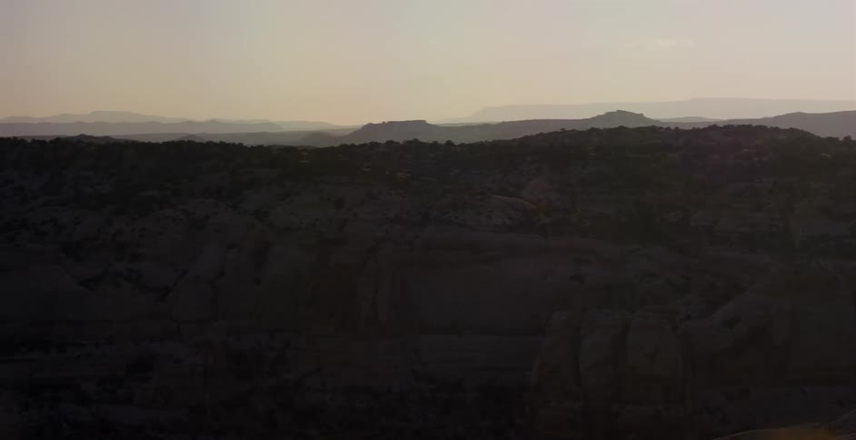 A slow pan across a silhouetted desert canyon landscape with rolling hills during a hazy golden hour