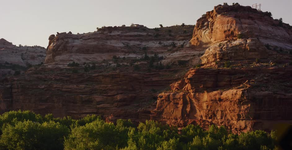Majestic red rock canyon walls glow in the warm golden hour light above a lush green forest