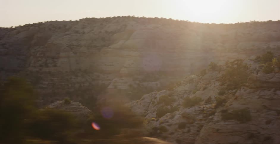 A motion-blurred shot reveals a sun-drenched desert canyon landscape from a moving car at sunset