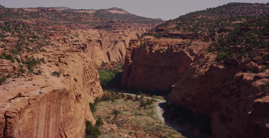 A slow reveal shot of a vast and majestic red rock canyon with a paved road running through the bottom