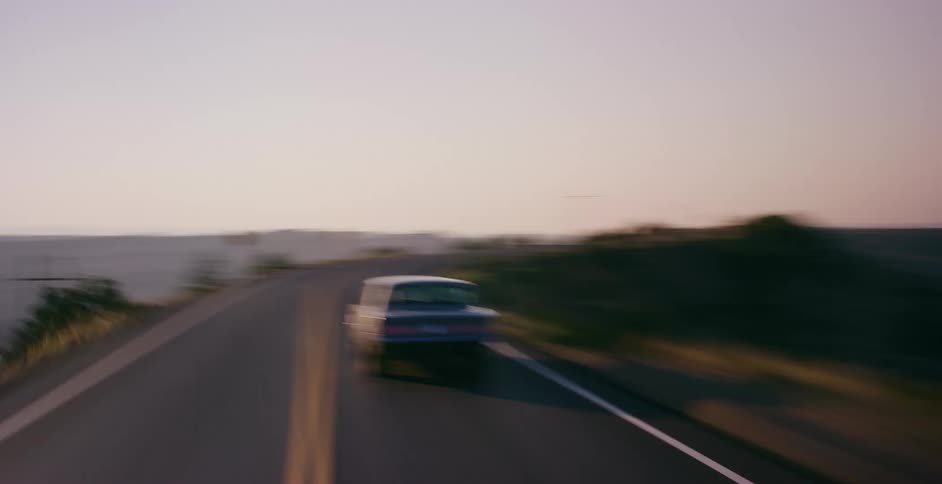 A classic American muscle car speeds down a winding desert highway during a beautiful sunset