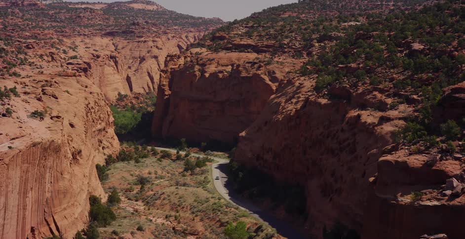 A car drives on a winding road through a majestic red rock canyon, revealed from behind a cliff face