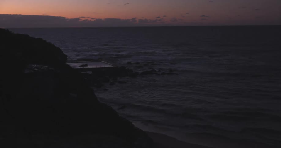 A serene view of a silhouetted coastline and ocean pool as gentle waves roll in at twilight