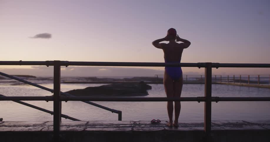 A serene woman prepares for an early morning swim in a beautiful tidal pool by the ocean at sunrise