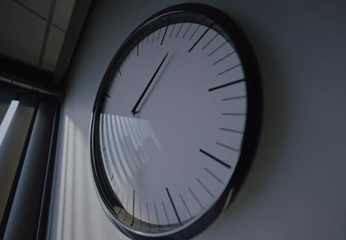 A minimalist wall clock speeds through a time-lapse as sunlight and shadows move across the wall, signifying the passage from day to night