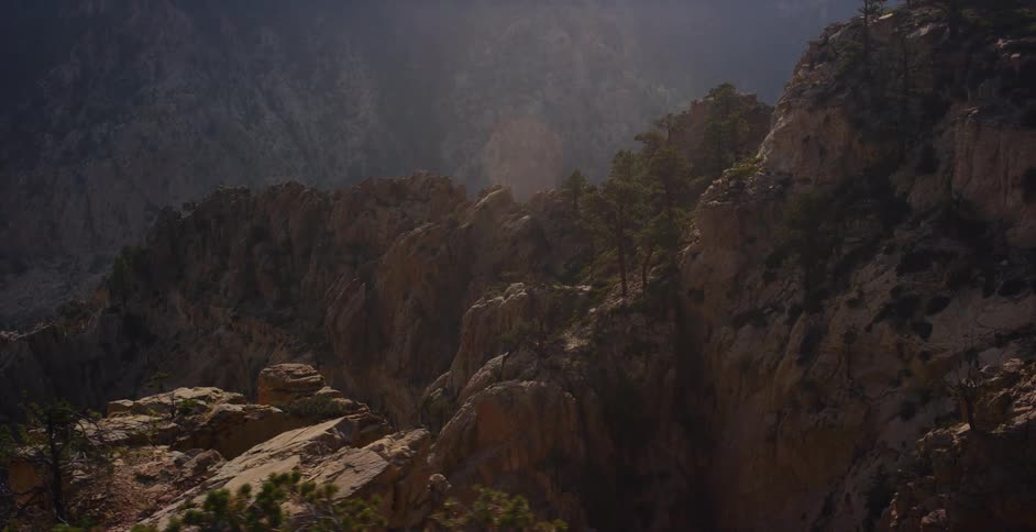 Slow cinematic pan reveals a vast and rugged mountain canyon landscape dotted with pine trees