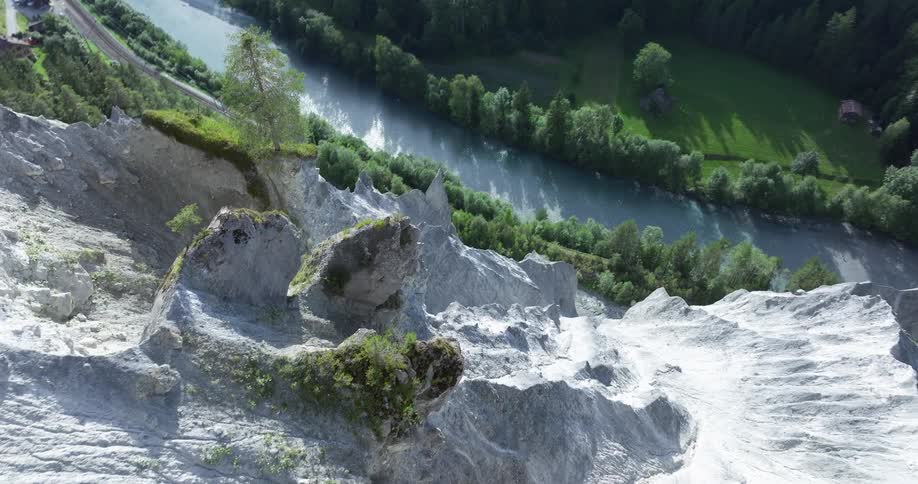 An aerial shot flies over a green mountain ridge to dramatically reveal the steep rocky cliffs of the Rhine River canyon below
