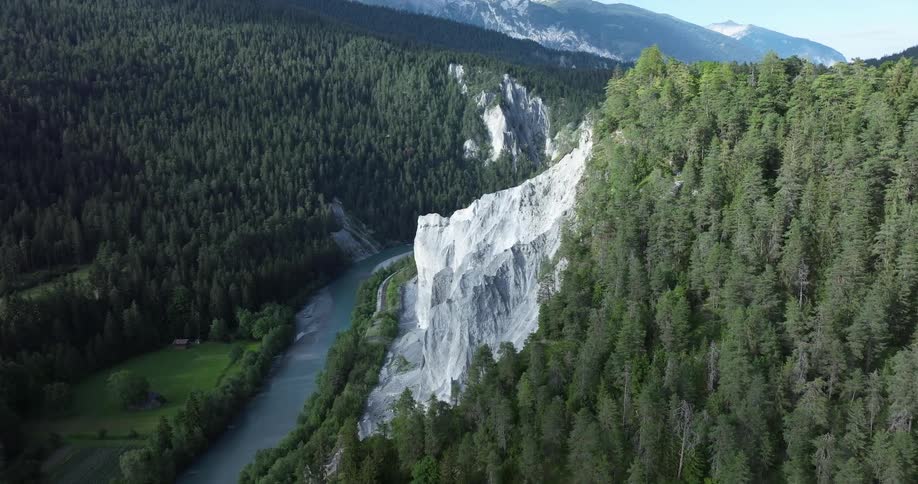 A majestic aerial view shows a river flowing through a deep canyon with dramatic white cliffs surrounded by a lush green forest
