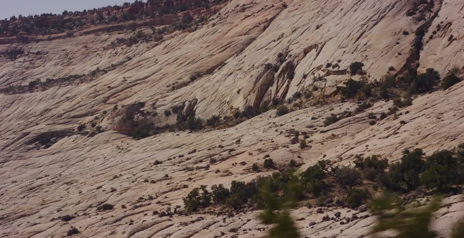 A slow tracking shot reveals the immense scale of a rugged, cracked sandstone mountainside in a remote desert landscape